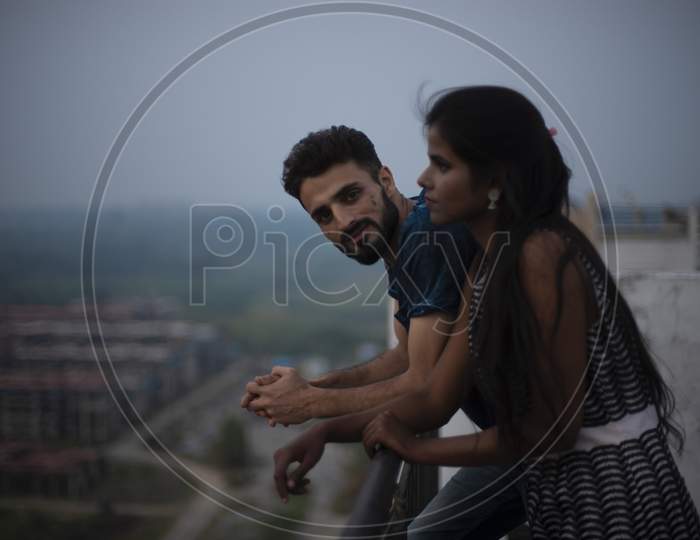 A dark skinned Indian/African girl in  western dress and a Kashmiri/European/Arabian man in casual wear spending time on a rooftop in the afternoon in urban background. Lifestyle of a couple.