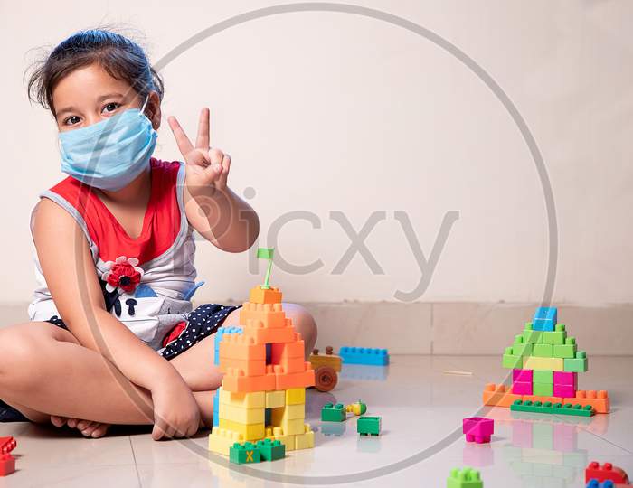Little Girl Showing Winning Sign In Fight Against Coronavirus With Mask On Face