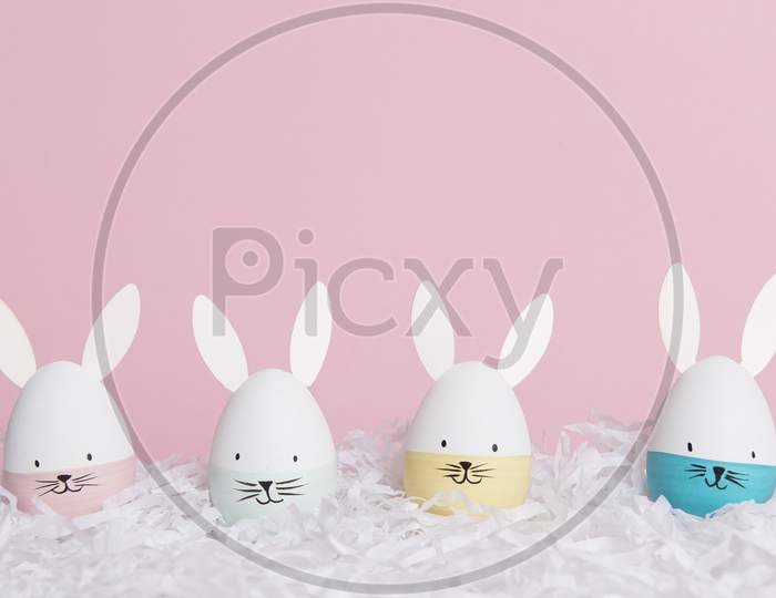 Easter Eggs With Bunny Faces In Nest On A Pink Background With Space For Copy