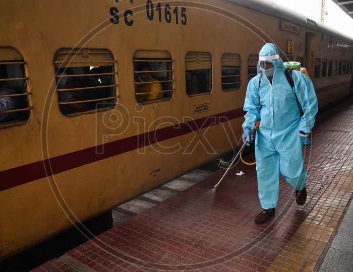 A worker wearing a PPE suit sprays disinfectant on the platform before the departure of a train to Secunderabad at Vijayawada Railway station as Indian Railways resumes train services, in Vijayawada.