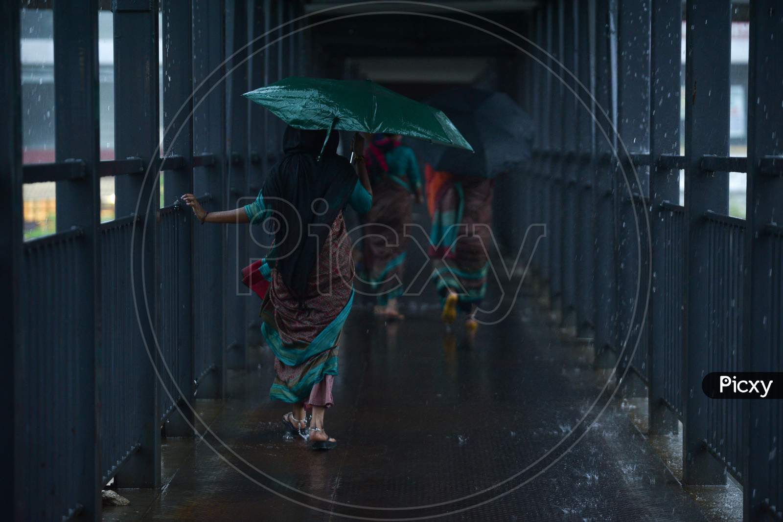 women walk on a foot over bridge as it rains heavily