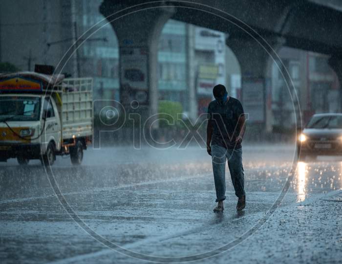 a masked man walks on the road as it rains heavily during the nationwide lockdown amid fears of coronavirus, may 31, 2020, Hyderabad