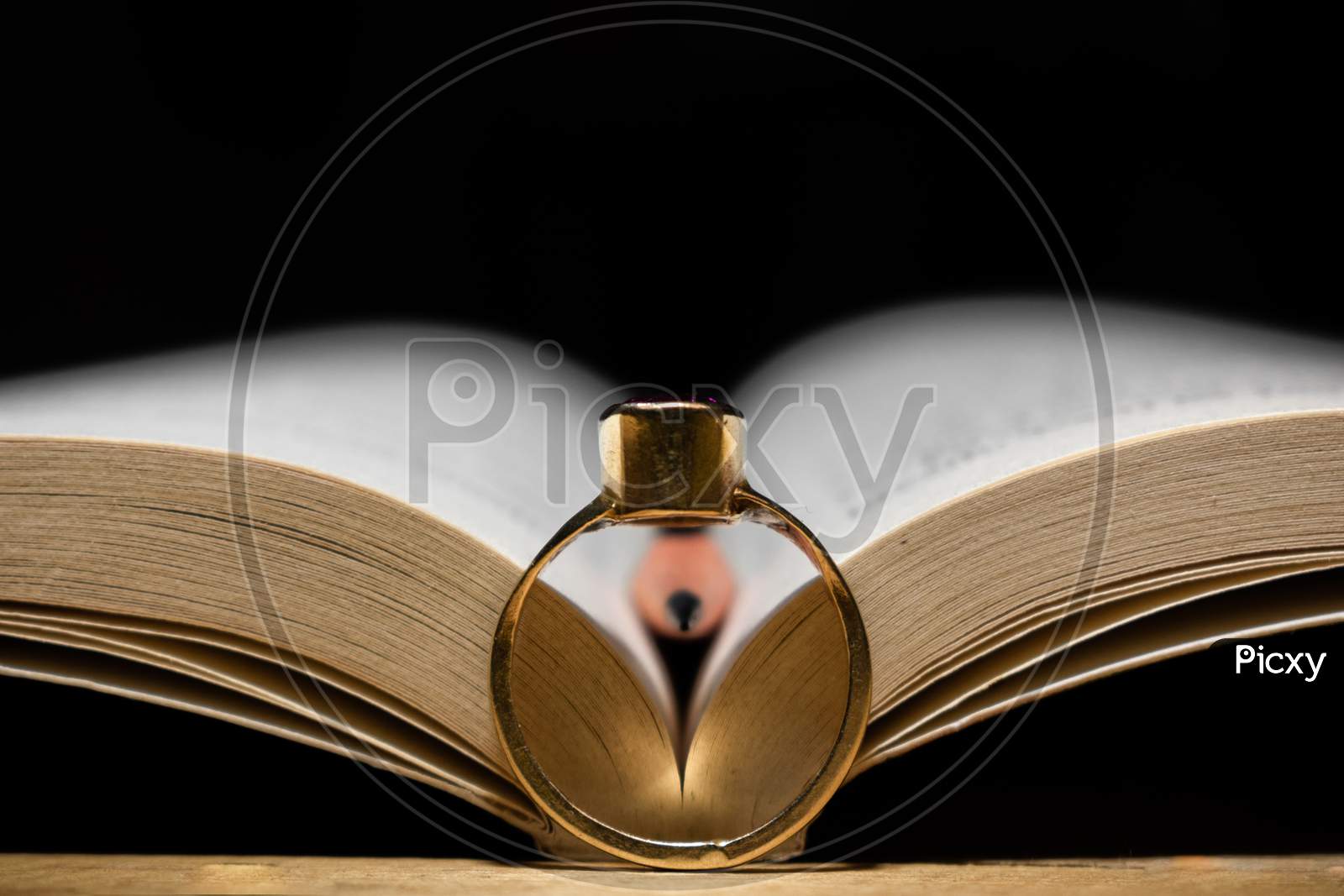 AN OPEN BOOK WITH A PENCIL AND A GOLDEN RING IN FRONT OF THAT