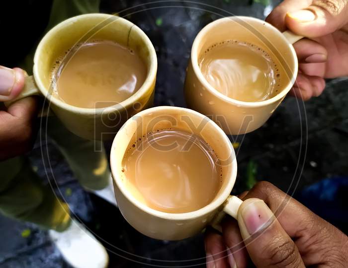 Cheering three friends with holding tea cups together by hands wet rainy climate. Lemon grass and ginger flavored healthy tea.