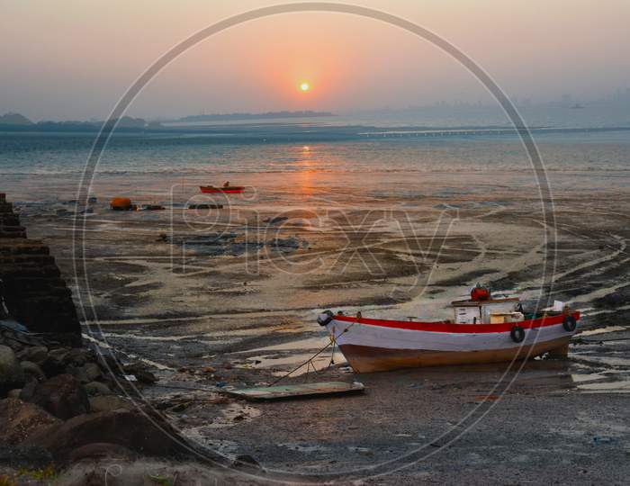 A Boat Anchored In The Ocean During Sunset In Low Tide.