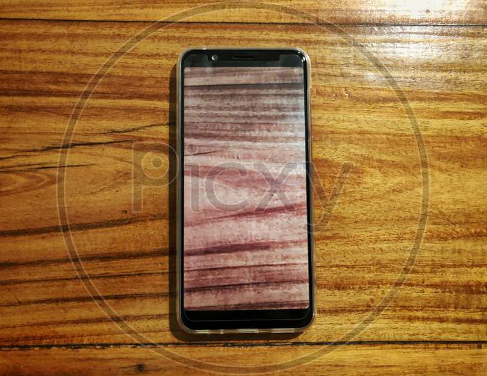 Black Smartphone On Wooden Background With Smartphone Screen Replicating The Same Wooden Texture.