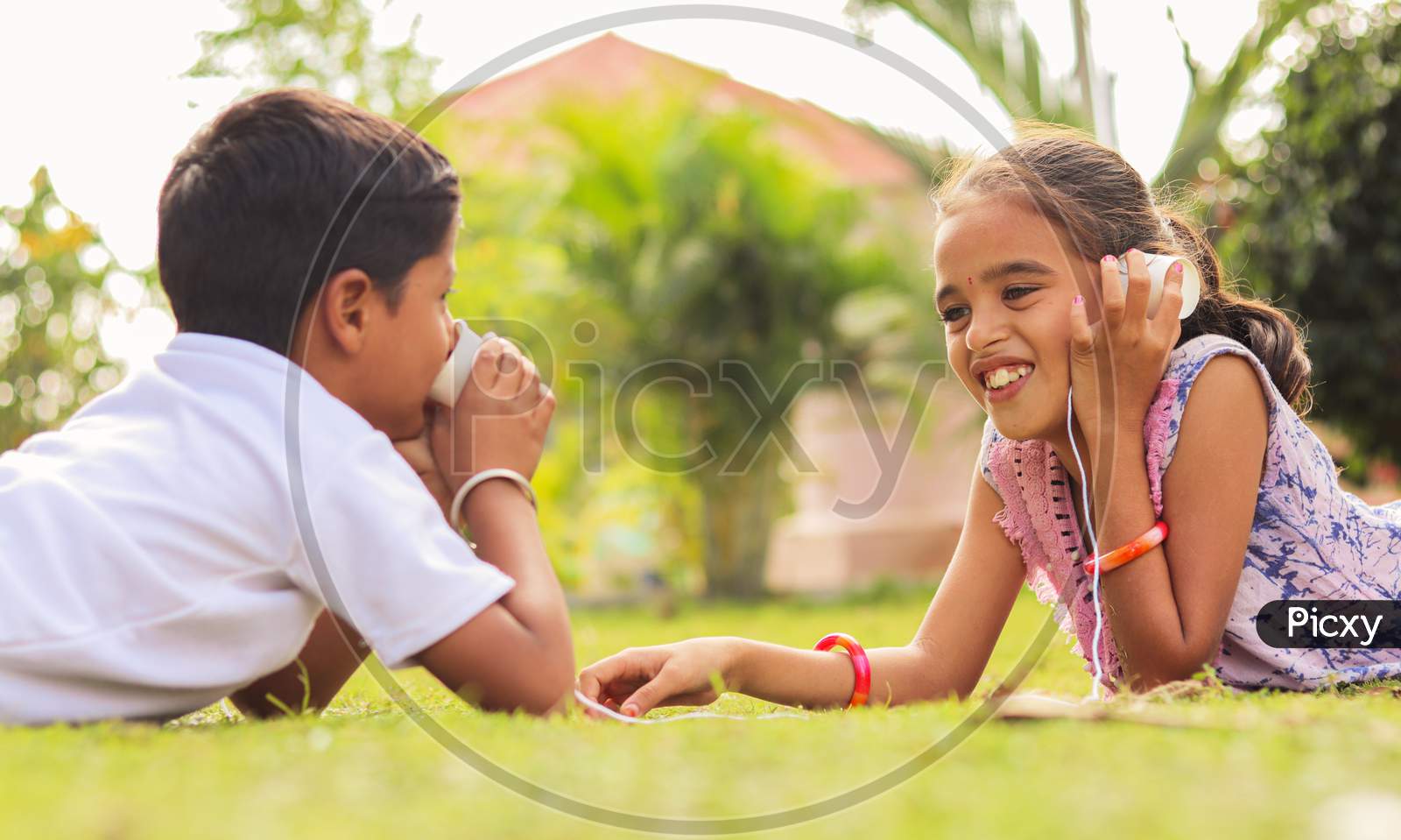 Two Children Having Fun By Playing With String Telephone At Park During Vacation - Concept Of Brain Development And Socializing By Playing Outdoor Games In The Technology Driven World.
