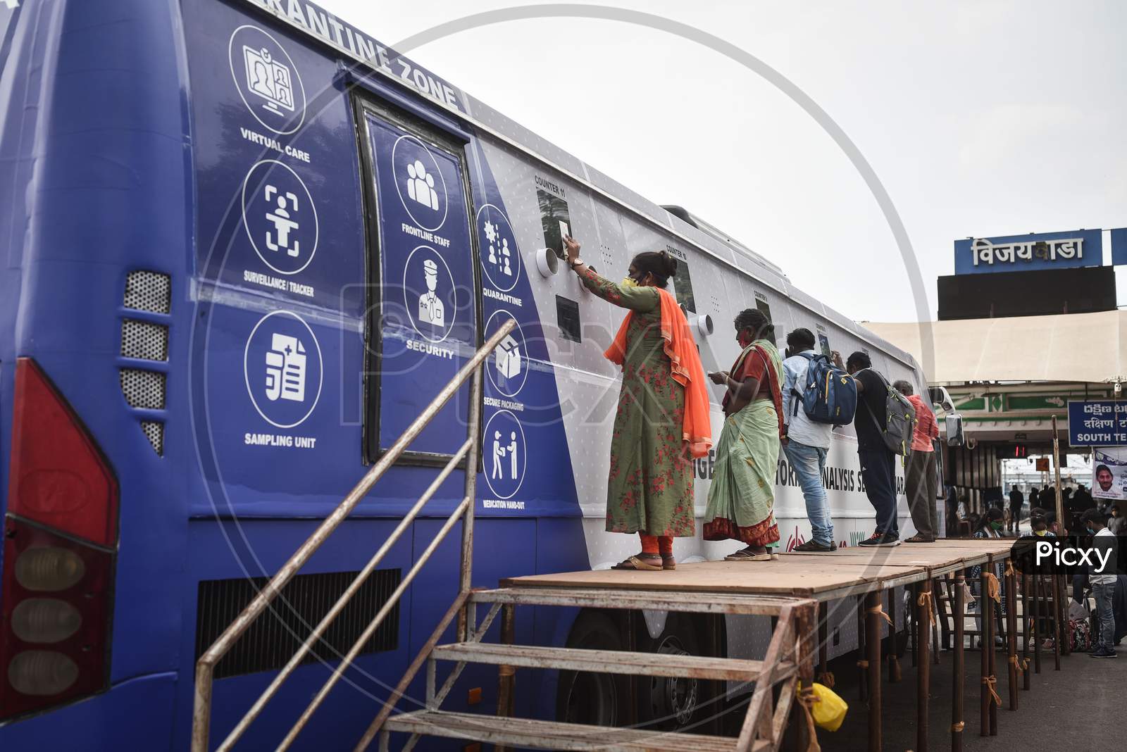 Passengers wait at a mobile swab collection bus, after their arrival at Vijayawada by Konark Express train, from a mobile swab collection bus, at Vijayawada Railway Station.