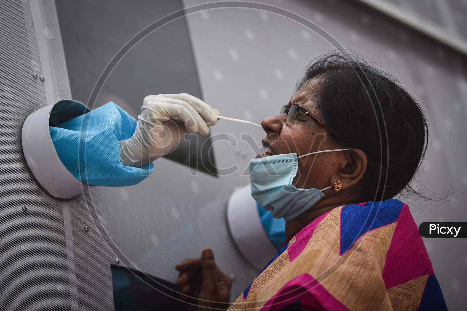 A healthcare worker collects a swab sample of a passenger who arrived at Vijayawada by Konark Express train, from a mobile swab collection bus, at Vijayawada Railway Station.