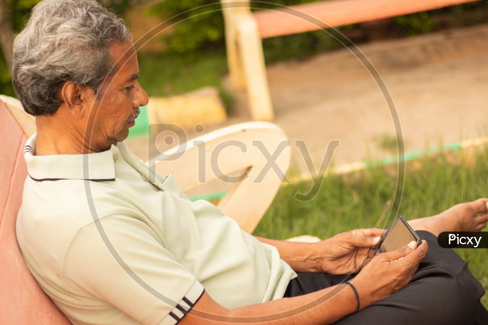 An old man or Elderly man using a Mobile Phone at Outdoors