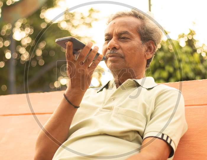An old man or Elderly man talking to a mobile-phone at the outdoors