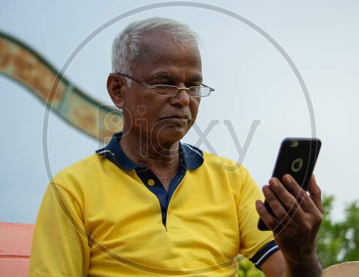 An Elderly Man Or Old Man using Smartphone or Mobile Phone At Outdoor