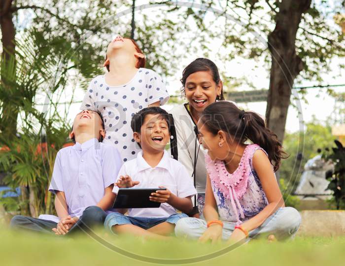 Group of Children using a Mobile or Smartphone and Laughing loudly in a Park or Outdoors