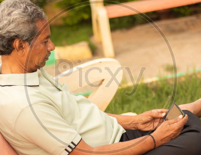 An old man or Elderly man using a Mobile Phone at Outdoors
