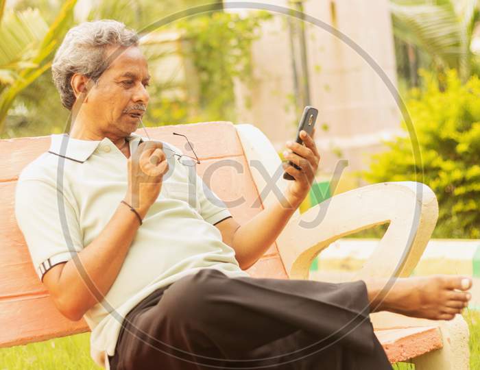 An old man or Elderly man talking to a Mobile Phone in a Park
