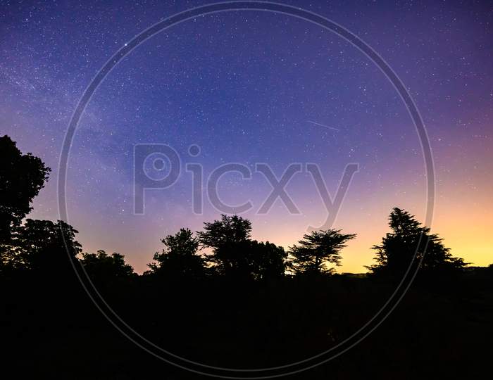 Colourful Long Exposure Star Filled Nightscape With Shooting Stars And Silhouette Trees In The Foreground