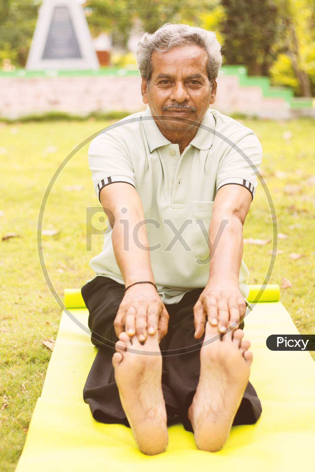 Low-Angle Full Length View Of A Old Man Sitting Down On Exercise Or Yoga Mat Touching His Toes - Concept Of Active Happy Elderly Health And Fitness