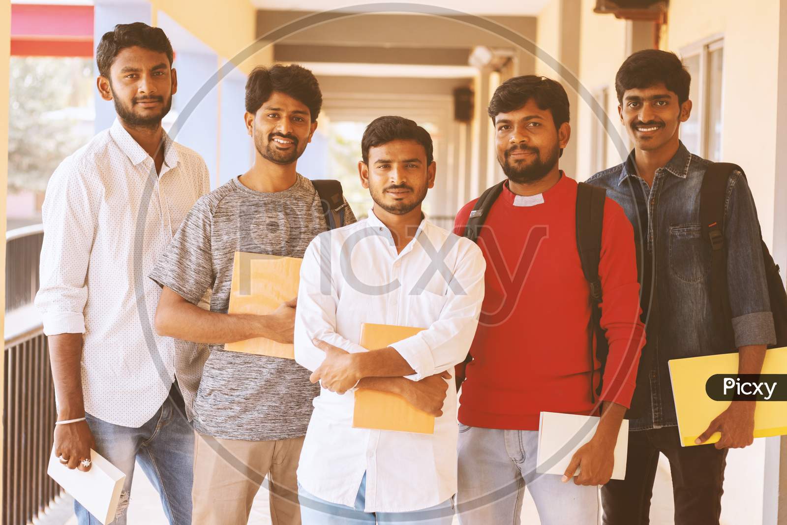 Happy Young Students Holding Books And Standing At College Corridor - Group Of Multiracial Confident Youth At University Campus - Concept Of Friendship, Togetherness And Student Life.