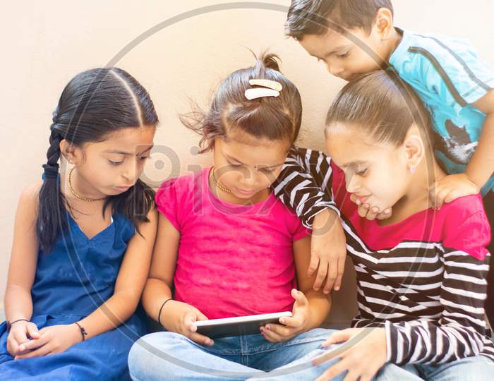 Group Of Four Cute Little Indian Kids Watching The Single Mobile Device