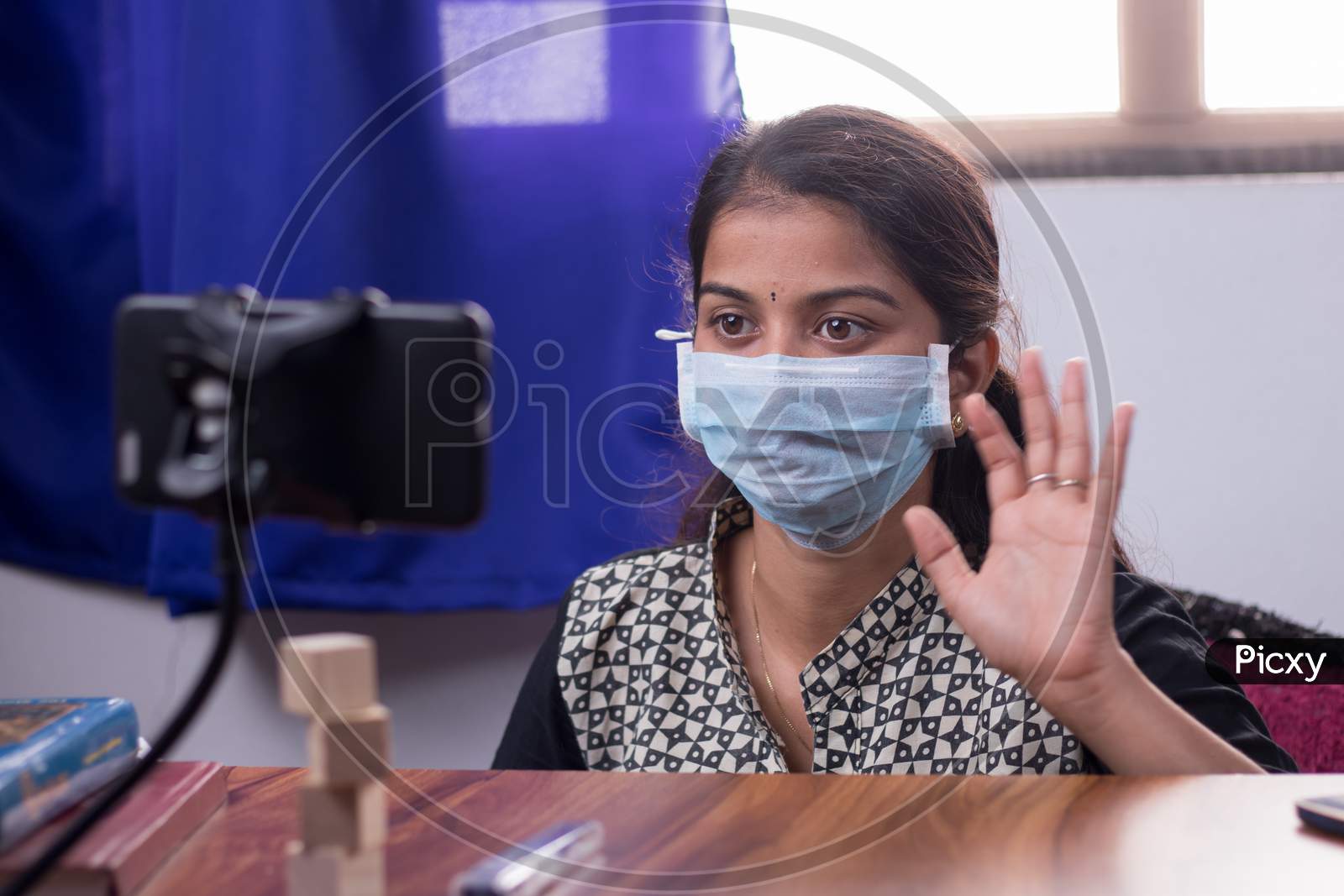 Concept Of Homeschooling And E-Learning, College Girl With Medical Mask Listing Virtual Class On Mobile During Covid-19 Or Coronavirus Pandemic Lock Down.