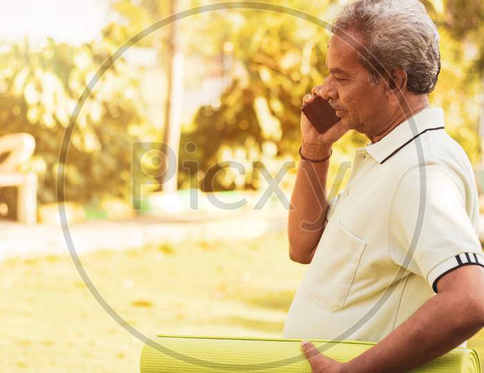 An old man talking on a Mobile Phone and holding Yoga mat in Hand