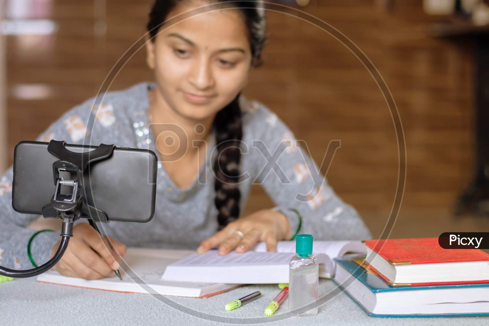 Selective Focus Of Mobile, Concept Of E-Learning At Home Due To Covid-19 Or Coronavirus Isolation - Young College Girl Taking Notes By Looking Into Virtual Class On Mobile Due To Isolation.