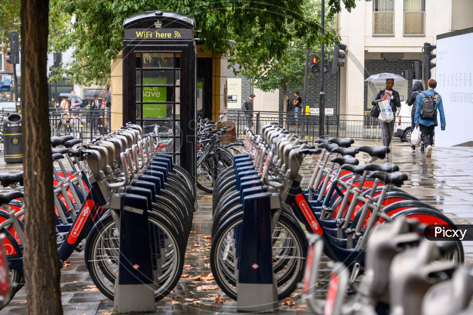Rows Of "Boris Bikes" For Hire Next To A London Free Wifi Here Black Telephone Box On The Strand On A Rainy Day
