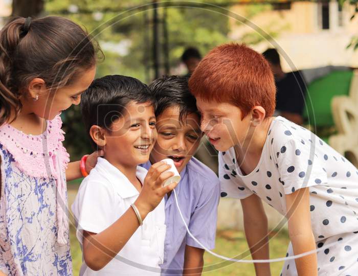 Children's Having Fun By Playing With String Telephone At Park During Vacation - Concept Of Brain Development And Socializing By Playing Outdoor Games In The Technology-Driven World.
