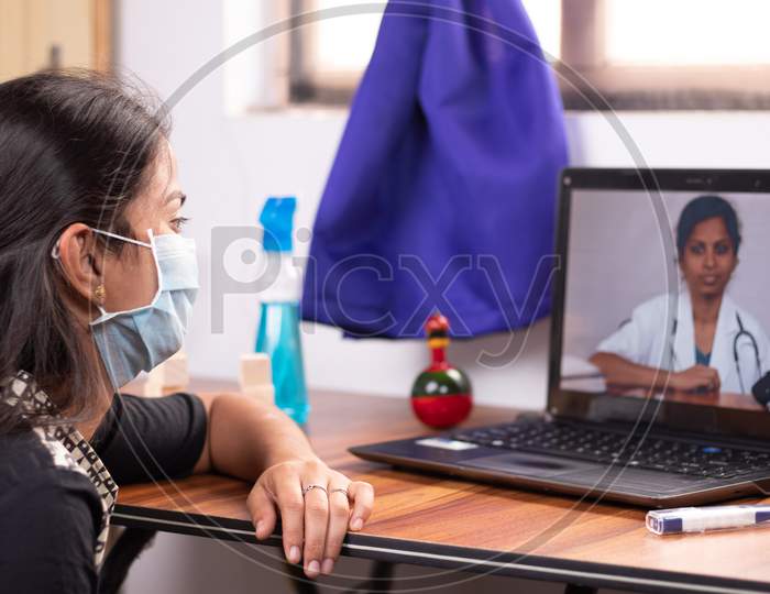 Concept Of Online Chat, Telehealth, Or Tele Counseling With Nurse Or Doctor On Screen During Coronavirus Or Covid-19 Pandemic - Girl In Medical Mask Listening To Doctor On Laptop At Home