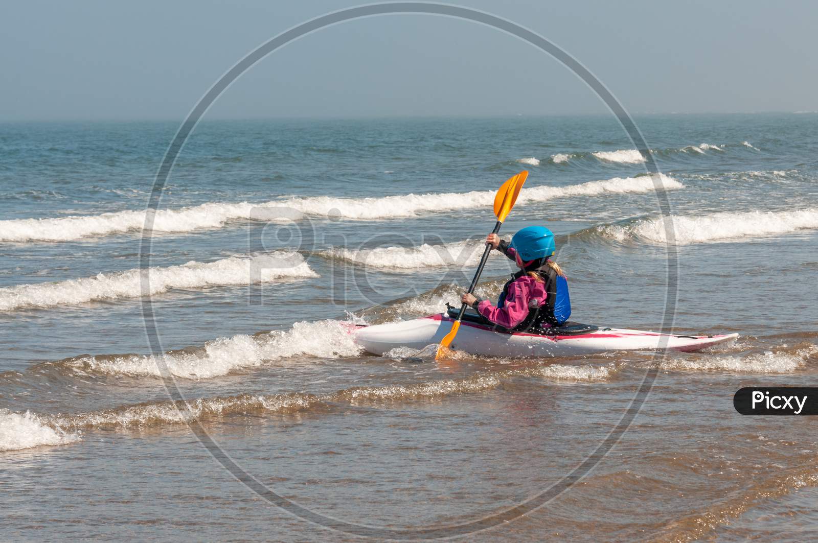 Young Girl Paddling Kayak Through Surf Out Towards The Sea On A Sunny Day