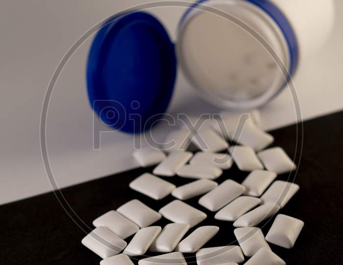 Gums in a bottle on a black and white background. Scattered chewing gum in the form of pads.