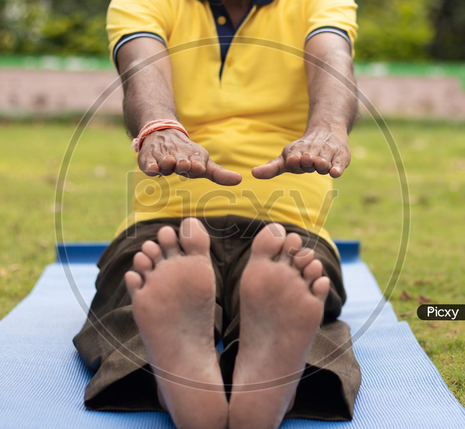 Low-Angle Full Length View Of A Old Man Sitting Down On Exercise Or Yoga Mat Touching His Toes