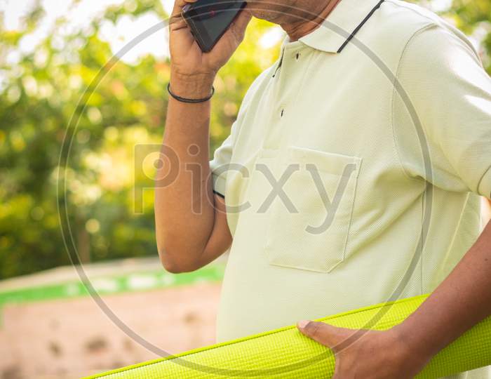An old man talking to a Mobile Phone and holding Yoga mat in Hand