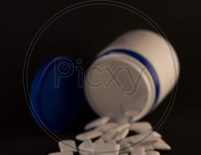 Gums in a bottle on a black background. Scattered chewing gum in the form of pads.