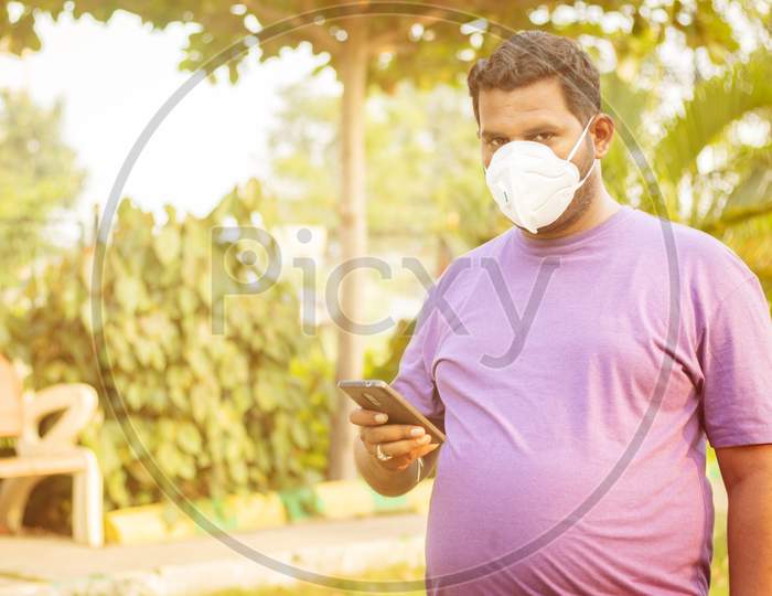 Portrait of a Young Indian Man using Mobile or Smartphone with Mask