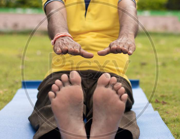 Low-Angle Full Length View Of A Old Man Sitting Down On Exercise Or Yoga Mat Touching His Toes