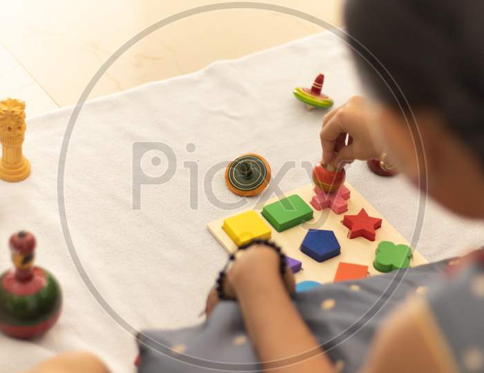 Focus On Hands Of Cute Little Child Girl Playing With Indian Wooden Channapatna Toys In The Room