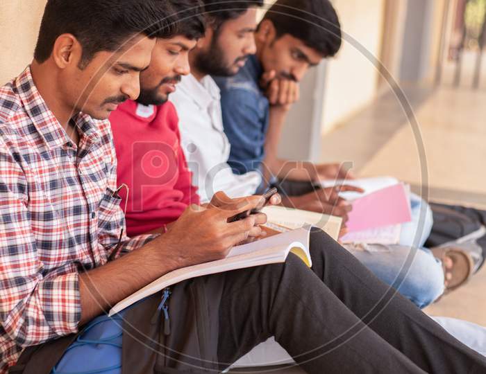 A student using a mobile phone while others are studying by Looking Into Books At College - Education, Learning Student, People Concept