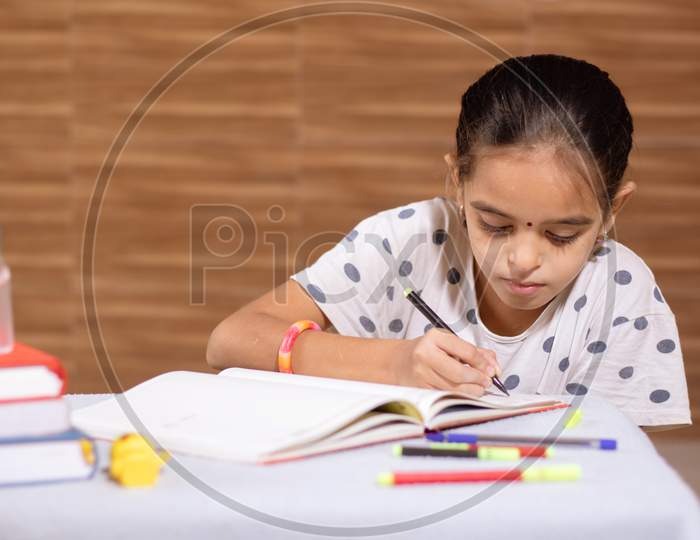 Little Schoolgirl Busy In Doing Homework With Hand Sanitizer In Front During Coronavirus Or Covid-19 Outbreak - Concept Of Homeschooling, Children Education