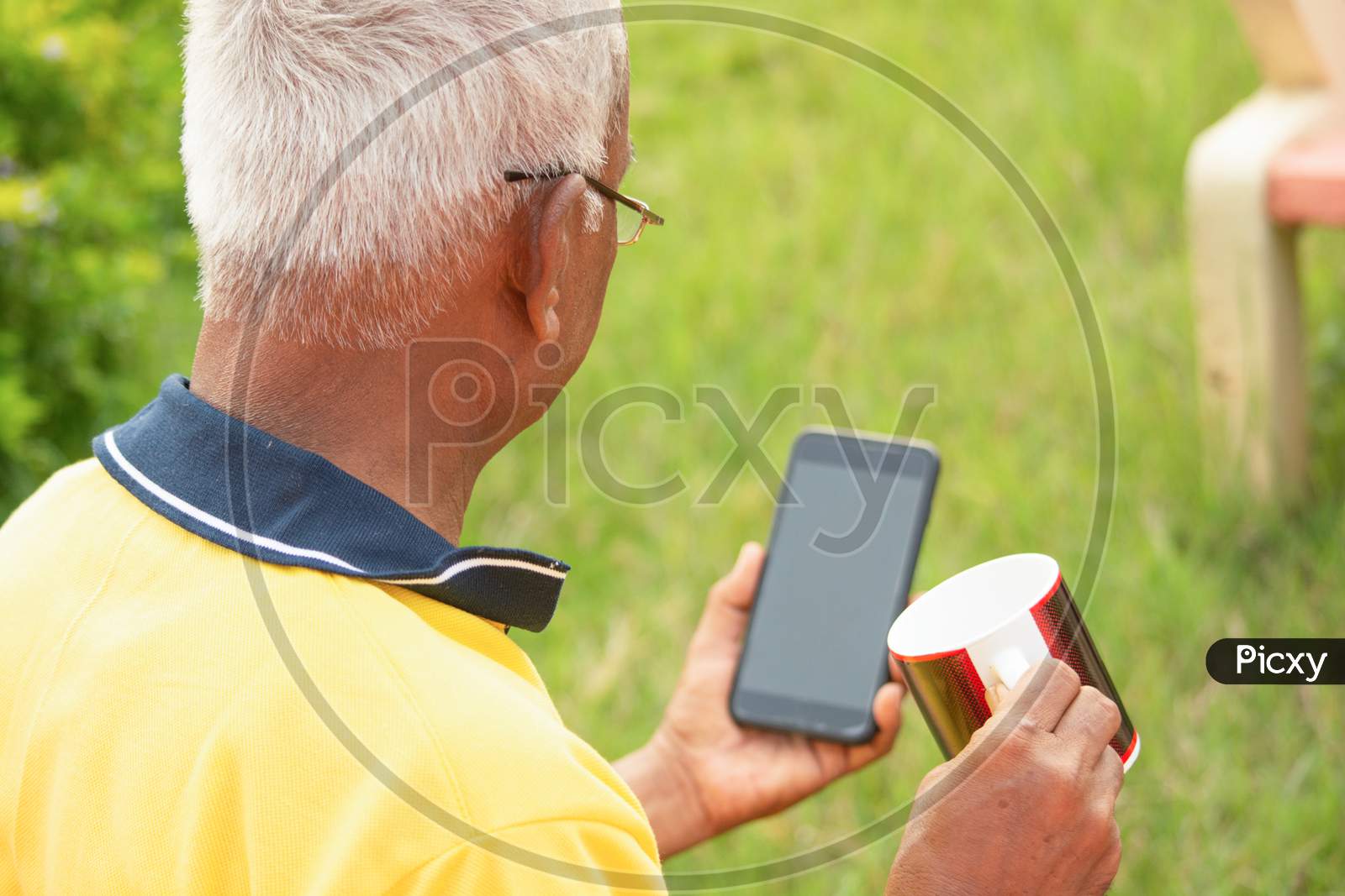 An old man or Elderly man using a mobile holding the cup in a park