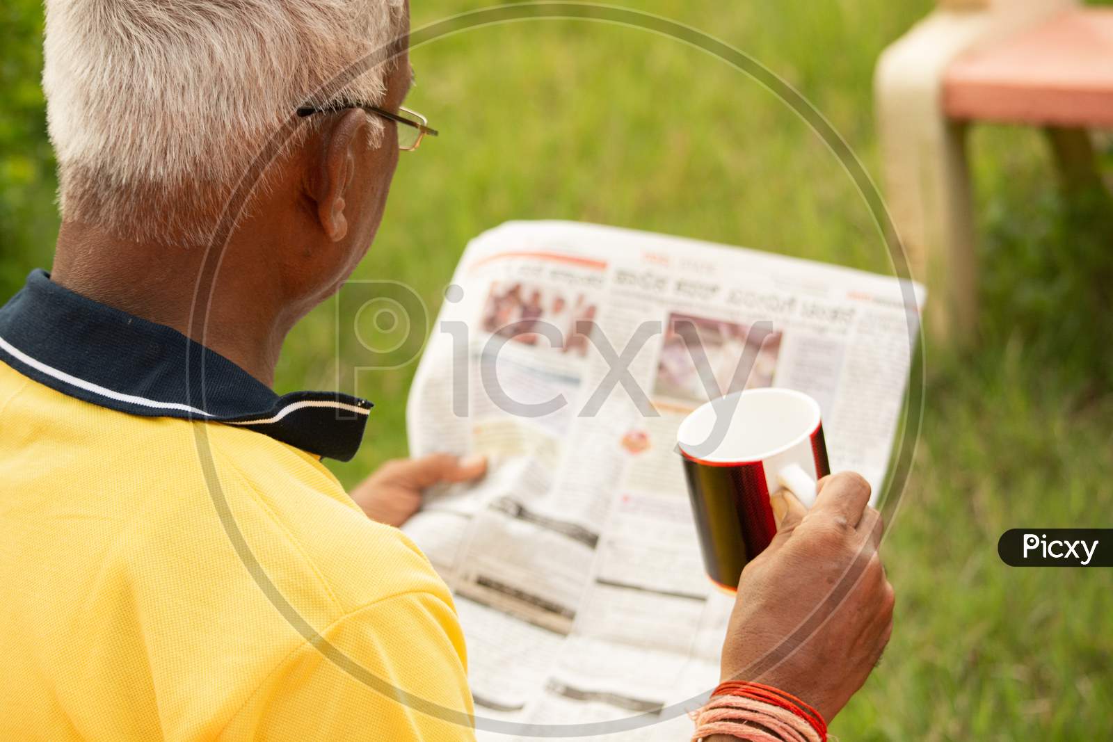An old man or Elderly man reading a newspaper holding the cup in a park