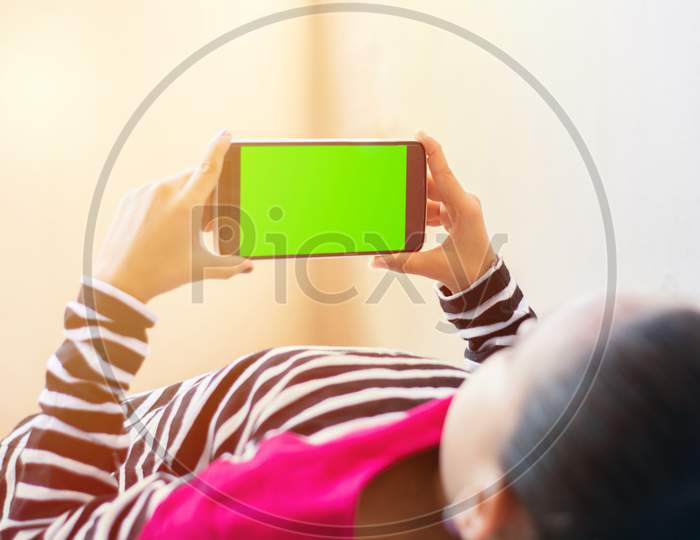 Little Indian Kid With Phone In Her Hands Sleeping On Bed, Mock Up With Green Screen, Focus On Phone.