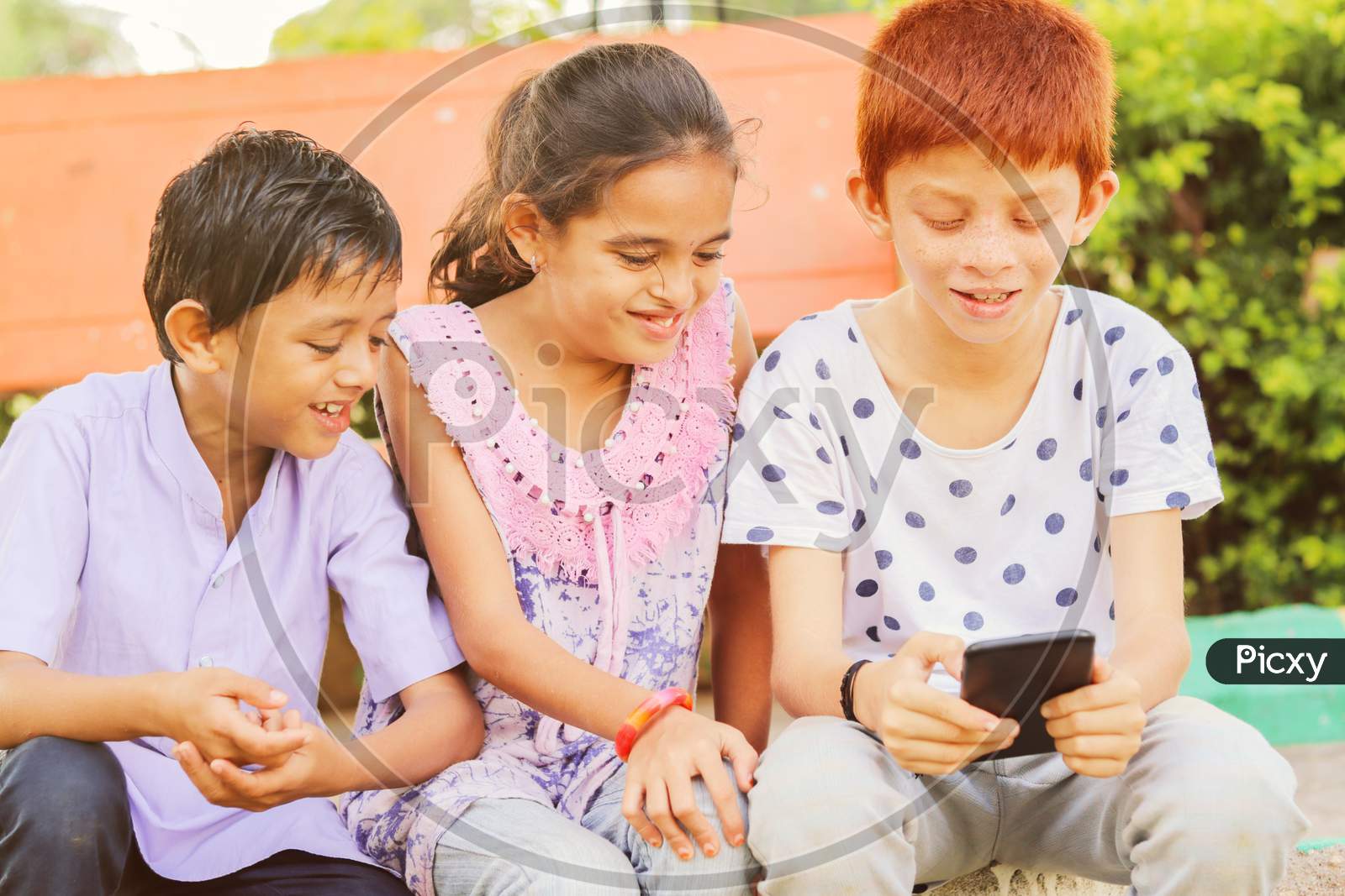 Children Busy In Using Mobile Phone At Park - Concept Of Kids On Mobile Devices And Technology Addiction - Young Teens Using Technology, Internet On Smartphone.