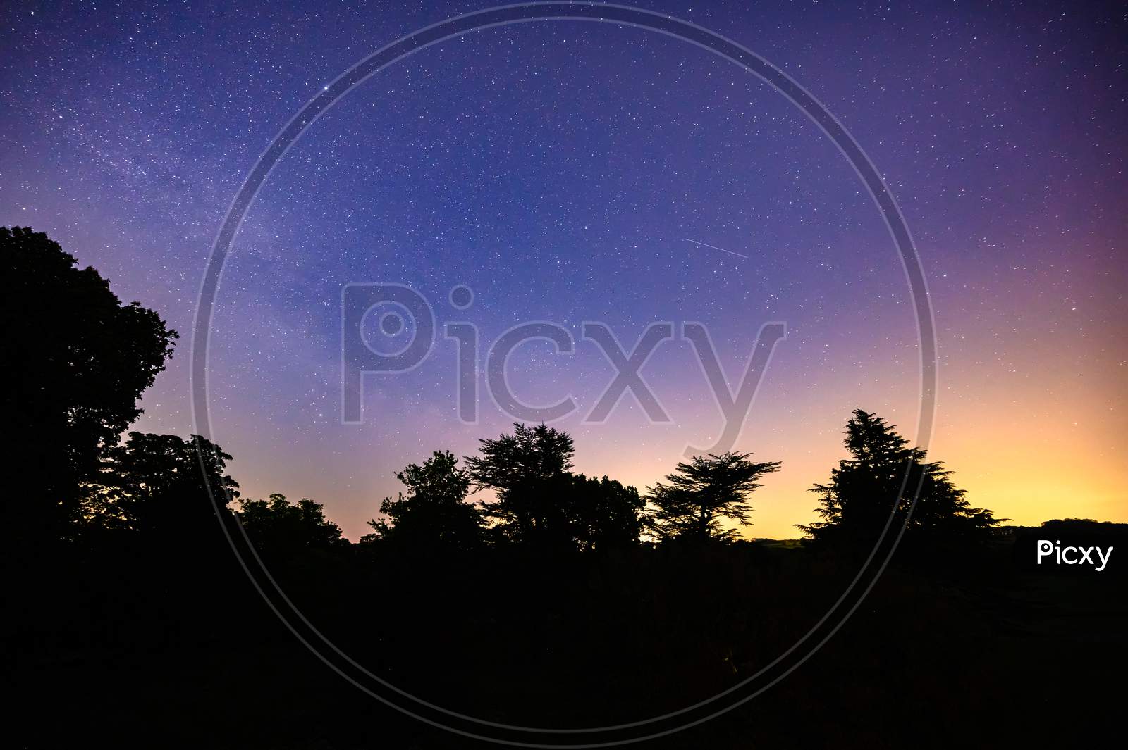Colourful Long Exposure Star Filled Nightscape With Shooting Stars And Silhouette Trees In The Foreground