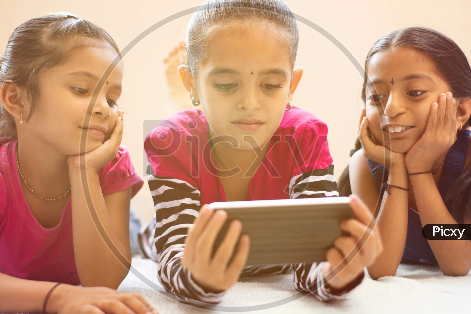 Three Cute Indian Children Watching Child Using Smartphone With Smiley Faces On Bed