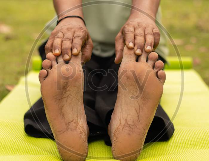 Low-Angle Full Length View Of A Old Man Sitting Down On Exercise Or Yoga Mat Touching His Toes