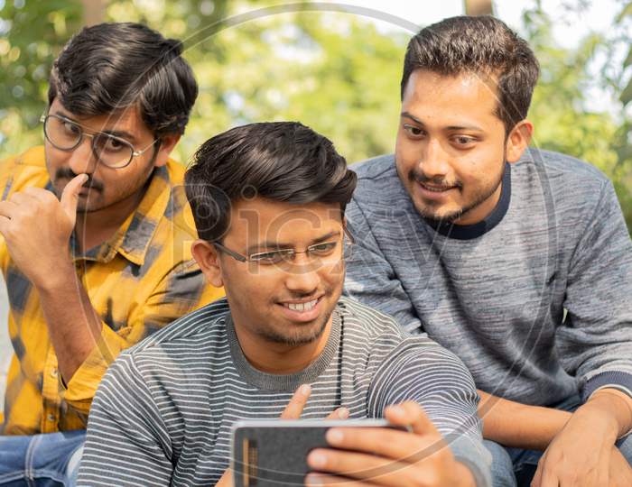 Group Of Happy Young College Students Using Mobile Phone At University Campus