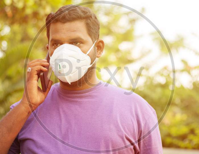 Concept Of Pollution, Radiation And Healthcare - Young Man Talking On Mobile With Air Pollution Mask, Outdoor - Indian Young Adult With Face Mask To Protect From Polluted Smog.