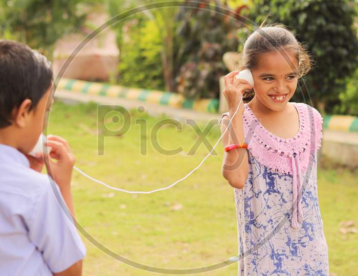 Two Children Having Fun By Playing With String Telephone At Park During Vacation - Concept Of Brain Development And Socializing By Playing Outdoor Games In The Technology Driven World.
