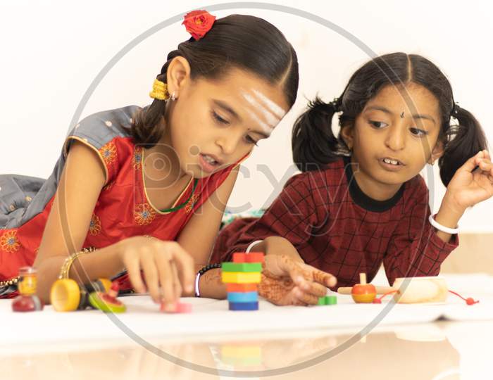 Interactively Two Indian Children Or Little Sisters Happily Playing With Colorful Wooden Toys Inside The Home.